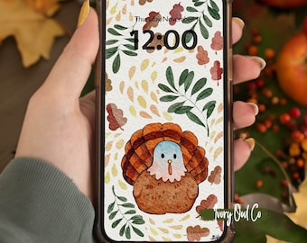 May include: A phone screen with a Thanksgiving-themed wallpaper featuring a cartoon turkey with a blue head and a brown body. The background is a white watercolor pattern with green leaves, brown acorns, and yellow and orange spots. The time is 12:00 and the date is Thursday, November 1. The text "Ivory Owl Co." is in the bottom right corner.