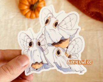 May include: Three cute cartoon bumblebees wearing ghost costumes. The bees are white with black stripes and have large, round eyes. The sticker has the text "Ivory Owl co" in the bottom right corner.