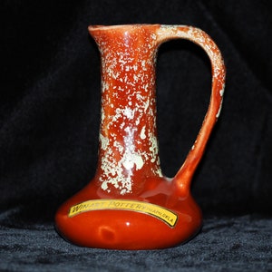 May include: A red ceramic pitcher with white speckles and a handle. The pitcher has a label that reads "Winart Pottery Miami, Okla."