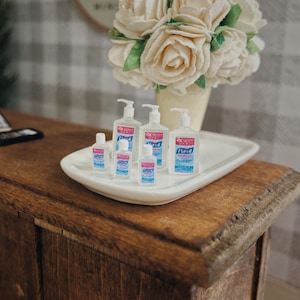 May include: A white tray with six bottles of hand sanitizer on a wooden surface. The bottles are labeled "Purell" and are various sizes. The bottles are clear and have a blue and pink label.