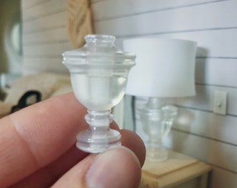 Op de afbeelding: Een heldere glazen lampenvoet met een decoratief ontwerp. De voet is klein en delicaat en zou perfect zijn voor een miniatuur poppenhuis of een feeëntuin.