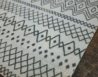 Może przedstawiać: Biała tkanina z czarno-białym geometrycznym wzorem. Wzór zawiera szereg rombów, zygzaków i kropek.