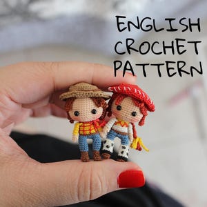 May include: Two small, crocheted dolls, one wearing a brown hat and the other a red hat, held in a hand. The dolls are dressed in colourful outfits, with the text "ENGLISH CROCHET PATTERN" above them. The dolls are approximately 5 cm tall.