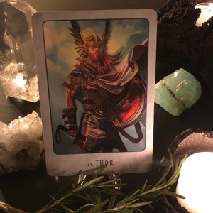 Peut inclure: Une carte de tarot repr&eacute;sentant Thor, un dieu nordique, tenant un marteau et un bouclier. La carte est num&eacute;rot&eacute;e 41 et le mot "THOR" est imprim&eacute; sous l'image.