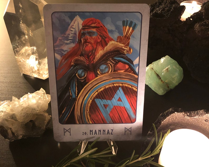 Peut inclure: Une carte avec un bouclier bleu et rouge avec un symbole de rune. La carte est d'un jeu de runes et est &eacute;tiquet&eacute;e "20. Mannaz".