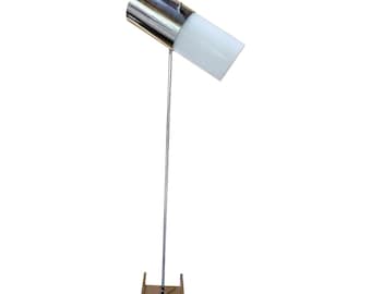 Pode incluir: Uma luminária de chão moderna com acabamento cromado e uma cúpula cilíndrica branca. A luminária tem um poste vertical e uma base retangular. A cúpula é inclinada, direcionando a luz para baixo. O design é minimalista e elegante.