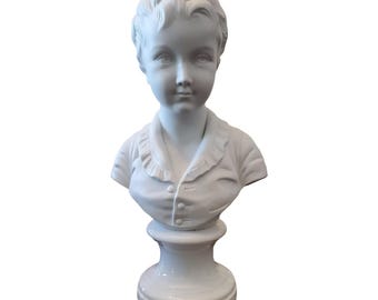 May include: White porcelain bust sculpture of a child with a ruffled collar. The bust is on a white pedestal.