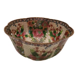 May include: A small, scalloped bowl with a white background and intricate floral designs in shades of pink, green, and blue. The bowl is made of metal and has a delicate, hand-painted look.