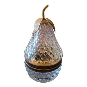 May include: A clear glass pear-shaped container with a gold metal top and leaf design. The container has a faceted design.