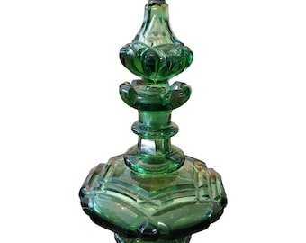 May include: A green glass bottle with a decorative, ornate stopper. The bottle has a faceted, geometric design.