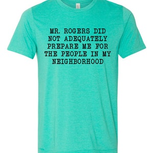 May include: A turquoise blue t-shirt with the text "Mr. Rogers did not adequately prepare me for the people in my neighborhood" printed in black.