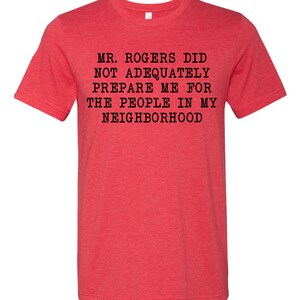 May include: Red t-shirt with black text that reads "Mr. Rogers did not adequately prepare me for the people in my neighborhood."