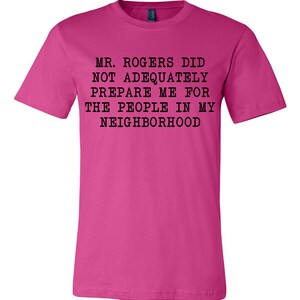May include: Pink t-shirt with black text that reads "Mr. Rogers did not adequately prepare me for the people in my neighborhood."