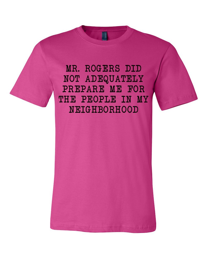May include: Pink t-shirt with black text that reads "Mr. Rogers did not adequately prepare me for the people in my neighborhood."