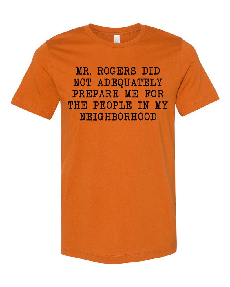 May include: Orange t-shirt with black text that reads "Mr. Rogers did not adequately prepare me for the people in my neighborhood."