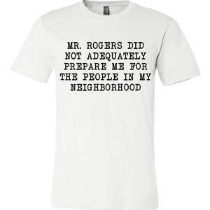 May include: White t-shirt with black text that reads "MR. ROGERS DID NOT ADEQUATELY PREPARE ME FOR THE PEOPLE IN MY NEIGHBORHOOD".