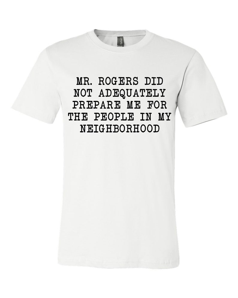 May include: White t-shirt with black text that reads "MR. ROGERS DID NOT ADEQUATELY PREPARE ME FOR THE PEOPLE IN MY NEIGHBORHOOD".
