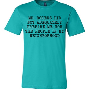 May include: A turquoise blue t-shirt with black text that reads "MR. ROGERS DID NOT ADEQUATELY PREPARE ME FOR THE PEOPLE IN MY NEIGHBORHOOD".