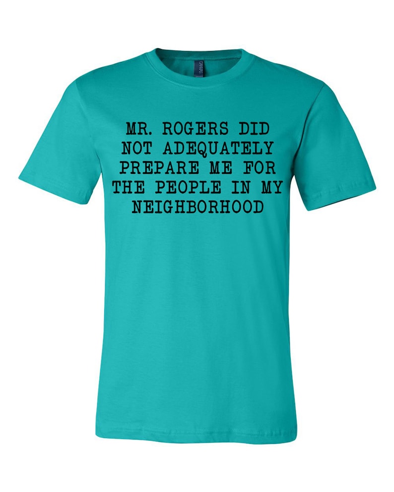 May include: A turquoise blue t-shirt with black text that reads "MR. ROGERS DID NOT ADEQUATELY PREPARE ME FOR THE PEOPLE IN MY NEIGHBORHOOD".