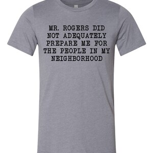 May include: A heather grey t-shirt with black text that reads "Mr. Rogers did not adequately prepare me for the people in my neighborhood."