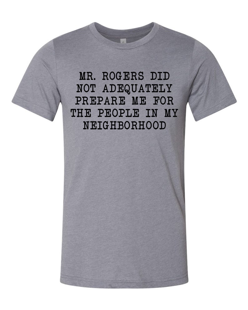 May include: A heather grey t-shirt with black text that reads "Mr. Rogers did not adequately prepare me for the people in my neighborhood."
