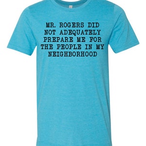 May include: A turquoise blue t-shirt with black text that reads "MR. ROGERS DID NOT ADEQUATELY PREPARE ME FOR THE PEOPLE IN MY NEIGHBORHOOD".