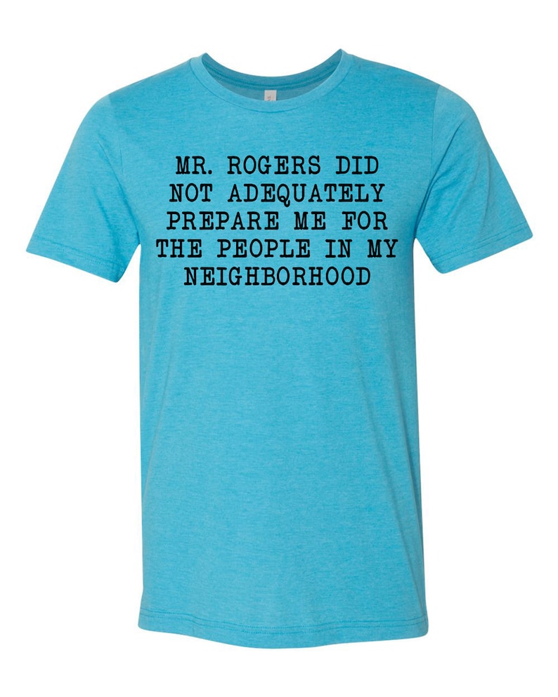 May include: A turquoise blue t-shirt with black text that reads "MR. ROGERS DID NOT ADEQUATELY PREPARE ME FOR THE PEOPLE IN MY NEIGHBORHOOD".