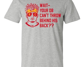 May include: Gray t-shirt with a red and yellow illustration of a football player wearing a helmet and sunglasses. The text "WAIT - YOUR QB CAN'T THROW BEHIND HIS BACK??" is printed on the shirt.