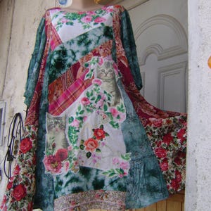 Pode incluir: Um vestido de patchwork com uma mistura de tecidos com padrões florais, secções axadrezadas e texturas tie-dye em tons de verde, rosa e branco. A peça inclui duas estampas gráficas de gatinhos rodeados por rosas e folhas verdes.