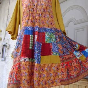 Puede incluir: Vestido patchwork en amarillo mostaza, rojo y azul con estampados florales. El vestido tiene mangas largas y cuello redondo. La falda está compuesta por varios parches con dobladillo con volantes. El vestido se exhibe en un maniquí.