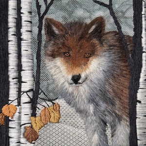 May include: Embroidered artwork featuring a detailed wolf peering through birch trees. The wolf has brown and gray fur with amber eyes. The birch trees have black and white bark, and there are a few brown and gold leaves.