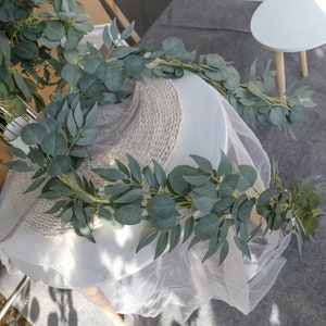 May include: A white sheer fabric draped over a woven base with a garland of green eucalyptus leaves.