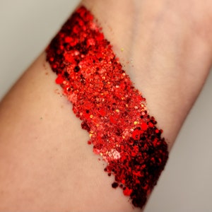 May include: A close-up of a person's arm with a thick stripe of red glitter applied to the skin.