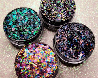 May include: Four small jars of glitter, each filled with a different color of iridescent glitter. The colors are green, black, purple, and orange.