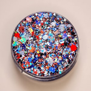 May include: A round container filled with colorful glitter. The glitter is a mix of red, blue, silver, and gold.
