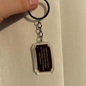 May include: Clear acrylic keychain with a black metal ring and chain. The rectangular charm has a dark brown border and text that reads "HERE YOU LEAVE TODAY AND ENTER THE WORLD OF YESTERDAY, TOMORROW AND FANTASY."