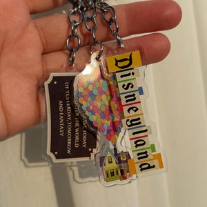 May include: Three keychains with silver metal rings. One keychain has the word "Disneyland" in colorful letters. Another keychain has a colorful balloon design. The third keychain has the text "OF YESTERDAY, TOMORROW AND FANTASY".