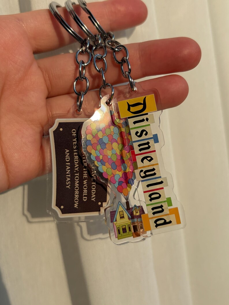 May include: Three keychains with silver metal rings. One keychain has the word "Disneyland" in colorful letters. Another keychain has a colorful balloon design. The third keychain has the text "OF YESTERDAY, TOMORROW AND FANTASY".