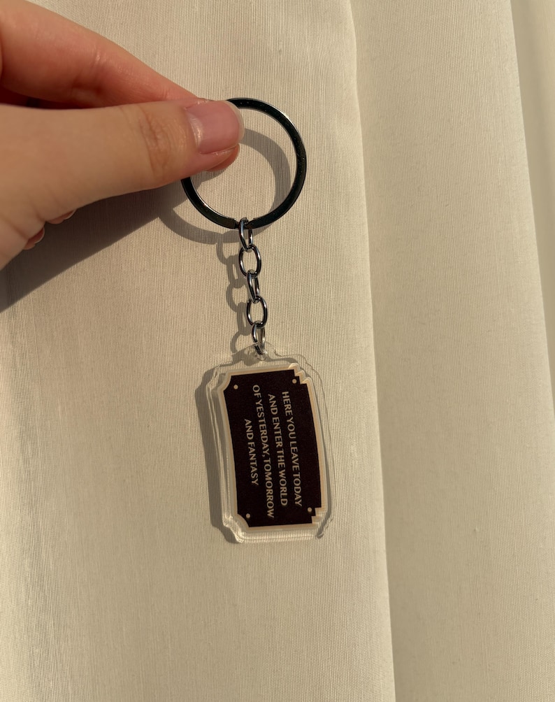 May include: Clear acrylic keychain with a black metal ring and chain. The rectangular charm has a dark brown border and text that reads "HERE YOU LEAVE TODAY AND ENTER THE WORLD OF YESTERDAY, TOMORROW AND FANTASY."