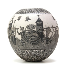 May include: A black and white ceramic sphere with a detailed design of skeletons and a tombstone with the inscription "Martha Ponce" and a Spanish inscription. The sphere is decorated with a floral pattern around the bottom.