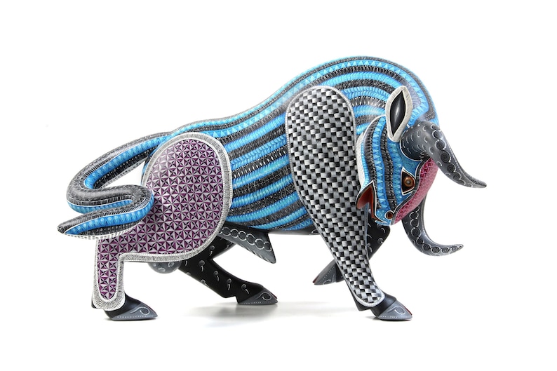 May include: A hand-carved wooden bull sculpture featuring intricate details. The bull is painted in shades of blue, black, white, and purple. The sculpture is a traditional Mexican folk art piece.