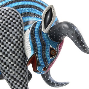 May include: A blue, black and white wooden bull sculpture with intricate details. The bull's head is lowered, and its horns are curled. The sculpture is painted with a variety of patterns, including stripes, swirls and dots.