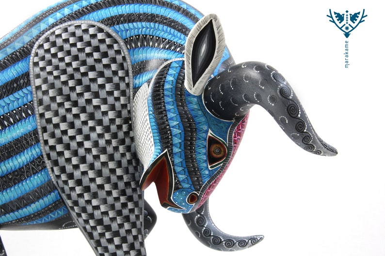 May include: A blue, black and white wooden bull sculpture with intricate details. The bull's head is lowered, and its horns are curled. The sculpture is painted with a variety of patterns, including stripes, swirls and dots.