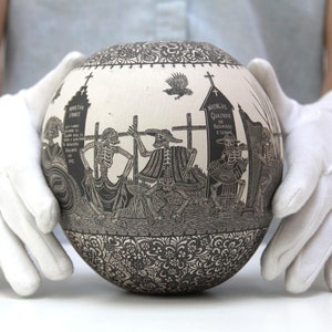May include: A white ceramic sphere with a black and white design depicting skeletons in a graveyard. The sphere is decorated with intricate floral patterns around the base.