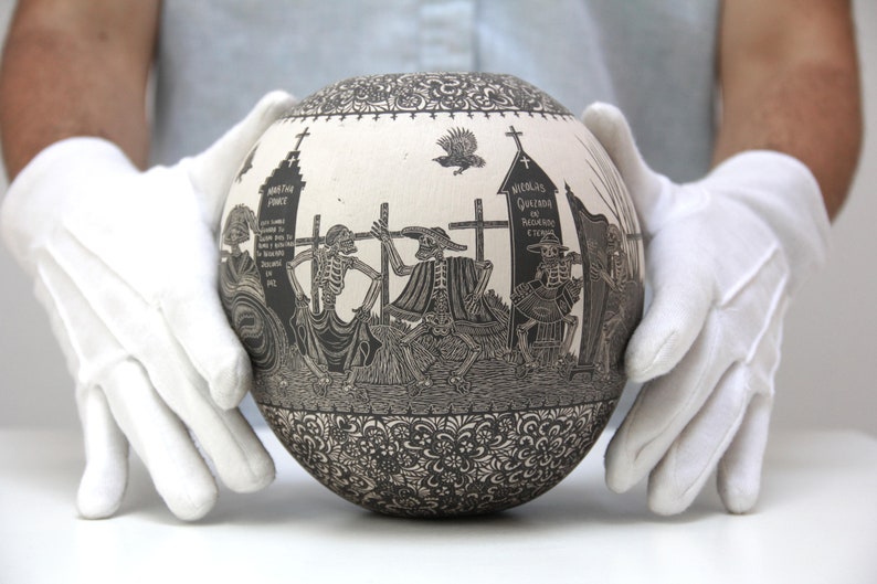 May include: A white ceramic sphere with a black and white design depicting skeletons in a graveyard. The sphere is decorated with intricate floral patterns around the base.