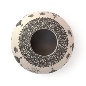 May include: A white ceramic pot with a black and white design. The pot has a round shape and a wide opening. The design features intricate patterns and symbols.