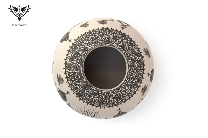 May include: A white ceramic pot with a black and white design. The pot has a round shape and a wide opening. The design features intricate patterns and symbols.