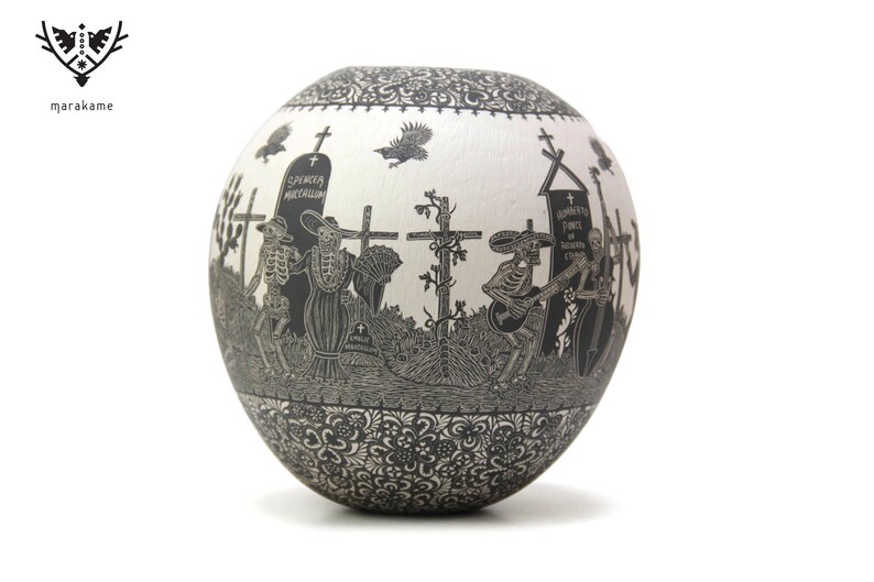 May include: A white ceramic pot with a black and white design of skeletons playing music and walking in a graveyard. The pot has a black and white floral design around the bottom.