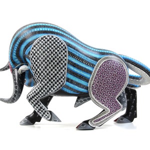 May include: A hand-carved wooden bull sculpture featuring intricate geometric patterns in blue, black, white, and purple. The bull is in a charging pose with its head lowered and horns pointed forward.
