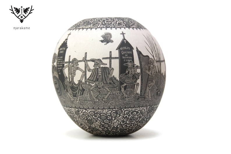 May include: A white ceramic sphere with a black and white design depicting skeletons in a procession. The design includes a cross, a tombstone with the text "NICOLAS QUELADA DE PADRON Y ESCRIBA", and a harp. The sphere is decorated with a black floral pattern around the edges.